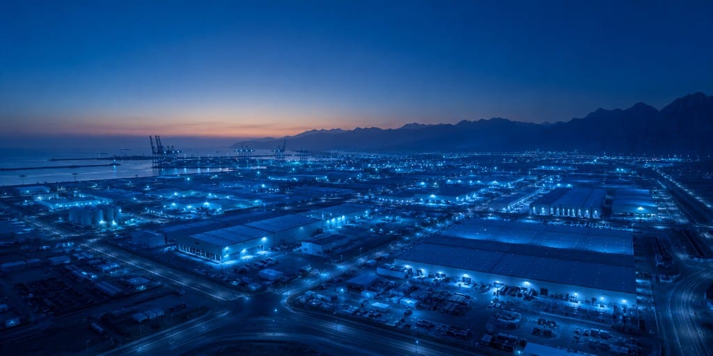 Aerial view of a major logistics and port hub at twilight with warehouse grid and waterfront cranes.
