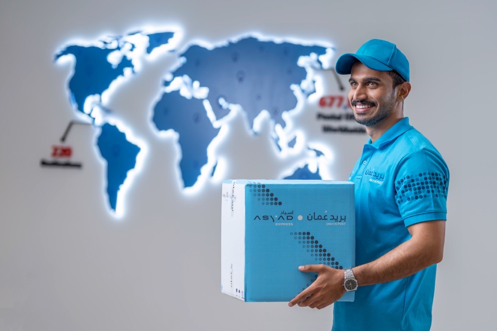 Oman Post and Asyad Express staff with a branded parcel in a retail environment.